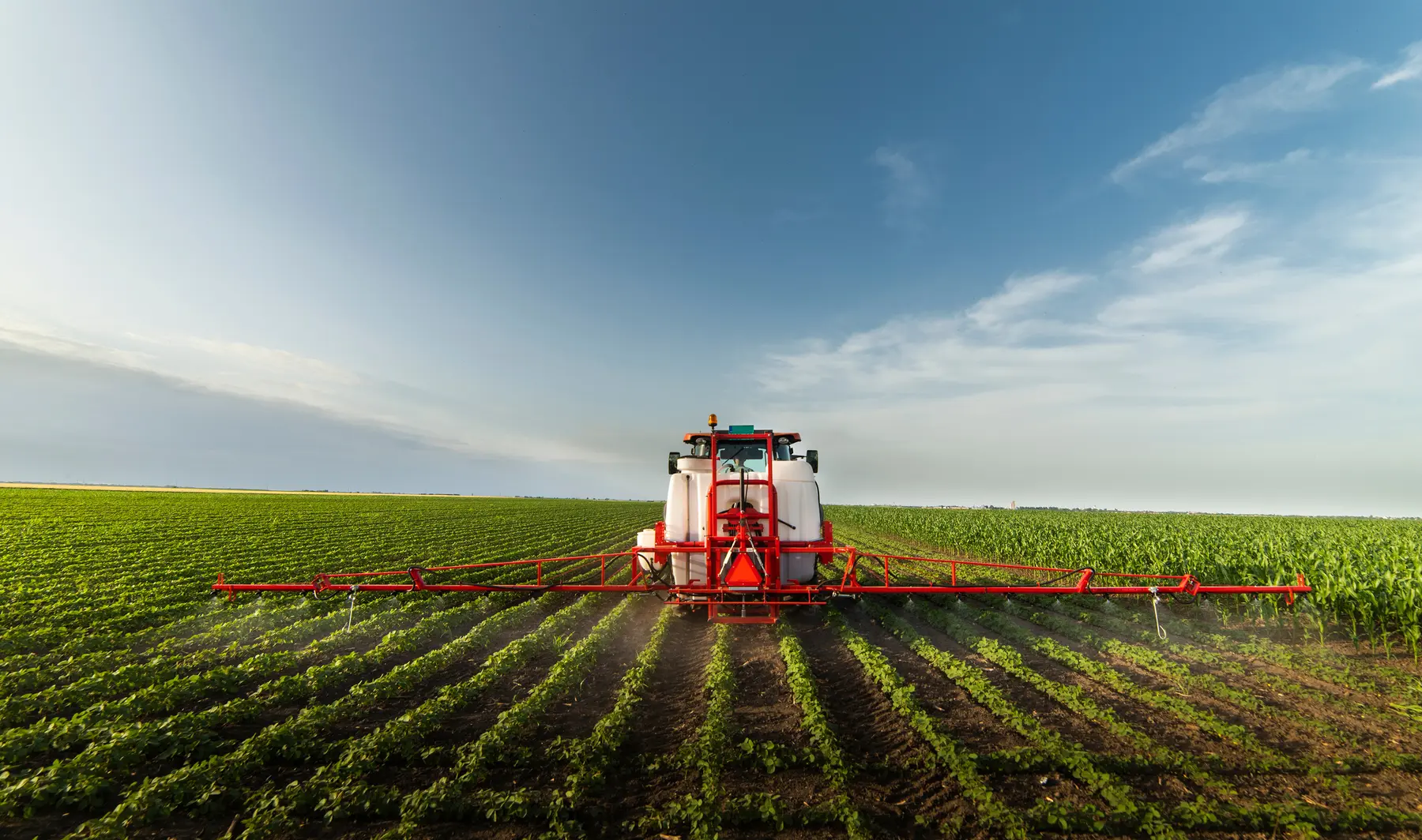 Hitched agricultural sprayer applying product across crop rows